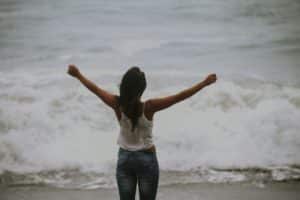 a woman raising her arms up facing the sea